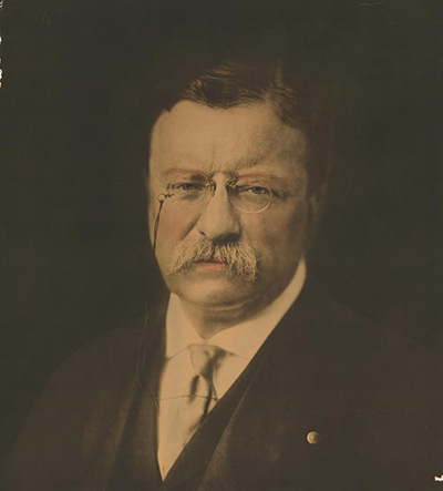 Sepia portrait of Roosevelt wearing a suit and glasses. His expression is serious.