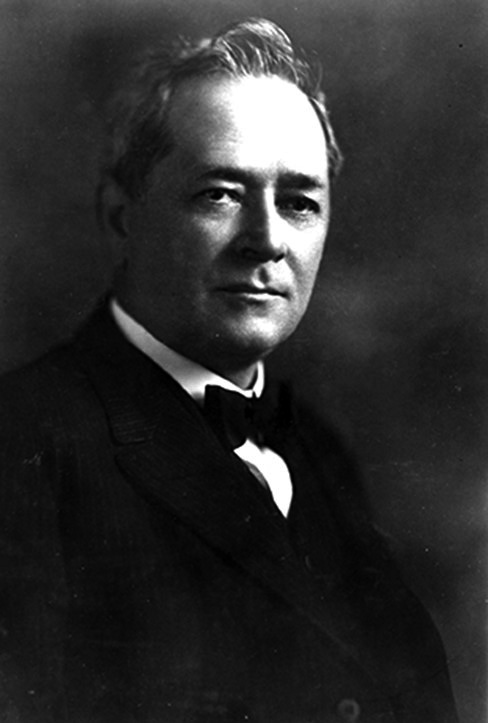 Black and white portrait of Charles Haskell with short cropped hair, suit, and bow-tie. 