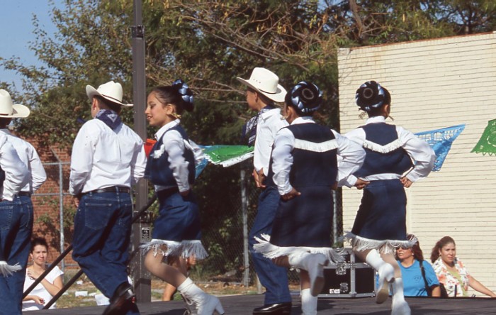 Children dance on stage. The boys wear jeans, boots, and cowboy hats, and the girls wear fringed denim skirts and tops.