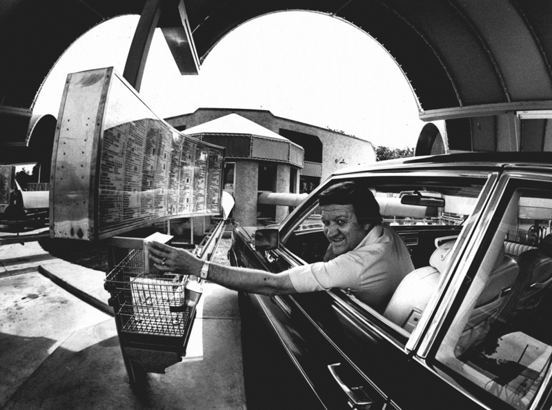A man leans out his car window, reaching to the order box. He turns to look at the camera.