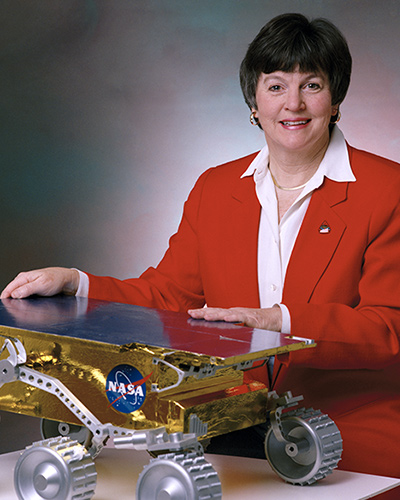 Shirley smiles as she rests her hands on a model of a rover.