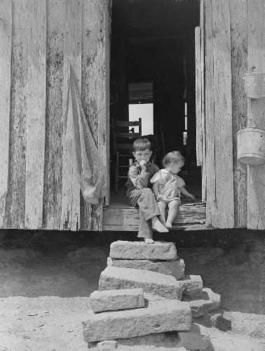 A child and baby sit in the door frame and above ramshackle steps