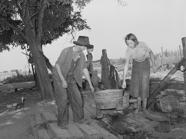 Two teenagers carry a washtub together. 