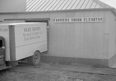 Frieght truck in front of a building with a sign, Farmers Union Elevator. 