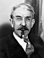 A closeup photo of a white man with a moustache in a suit smoking a cigar.