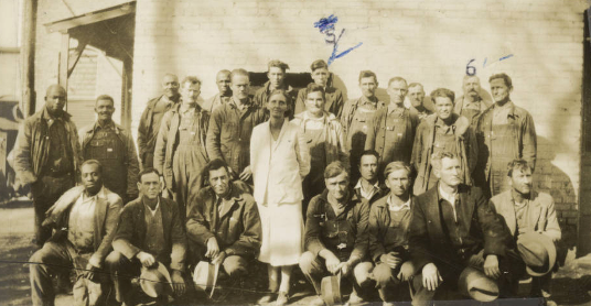 One white woman stands in front of a group of men, both Black and white, both standing and squatting to take the photo. 