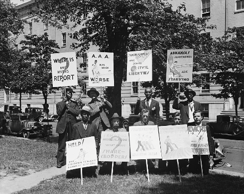 A group of white and black men hold protest signs outside of a building.  