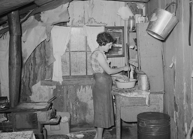 A white woman in a ranshacle house working in the kitchen area. 