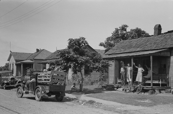 A street scene with two trucks and three houses. On the nearest house, four people wave goodbye at one of the trucks. 