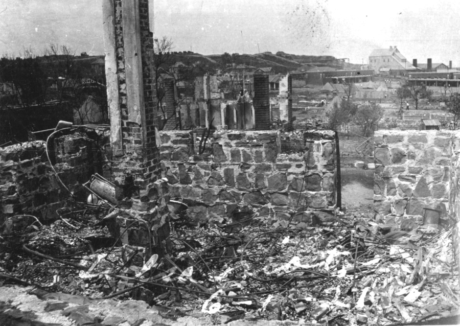 Burned wires and debris inside of short stone walls. Buildings are visible in the distance and handwriting reads, Tulsa riot 6-1-21