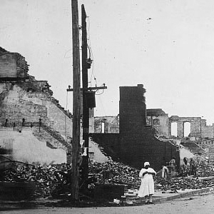 A Black woman dressed in white stands in the rubble of the buildings destroyed during the massacre