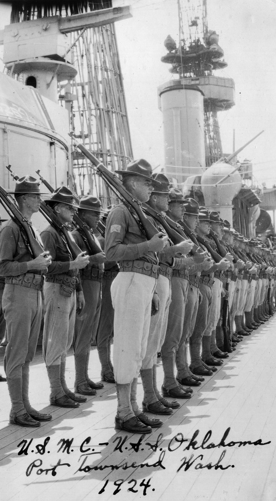 Soldiers in formation with rifles on their shoulders on the deck of the USS Oklahoma.