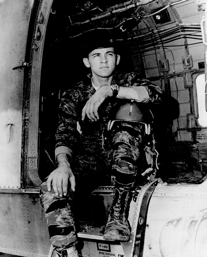 A man in a uniform and beret sits in the opening of an aircraft looking into the distance.