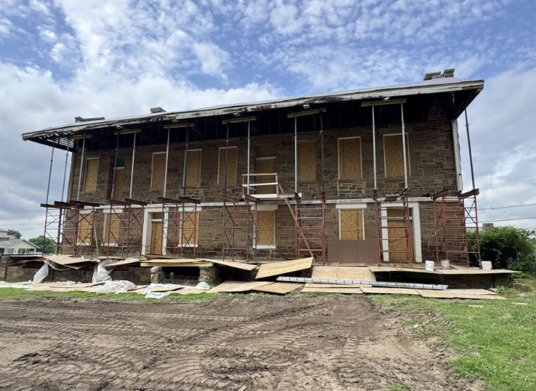 The exterior of the barracks with scaffolding and wood covering the first-floor deck. The second-floor balcony has been removed.