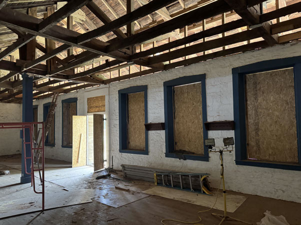 Inside view of the barracks showing ceiling beams and supports and window openings with temporary wood coverings.
