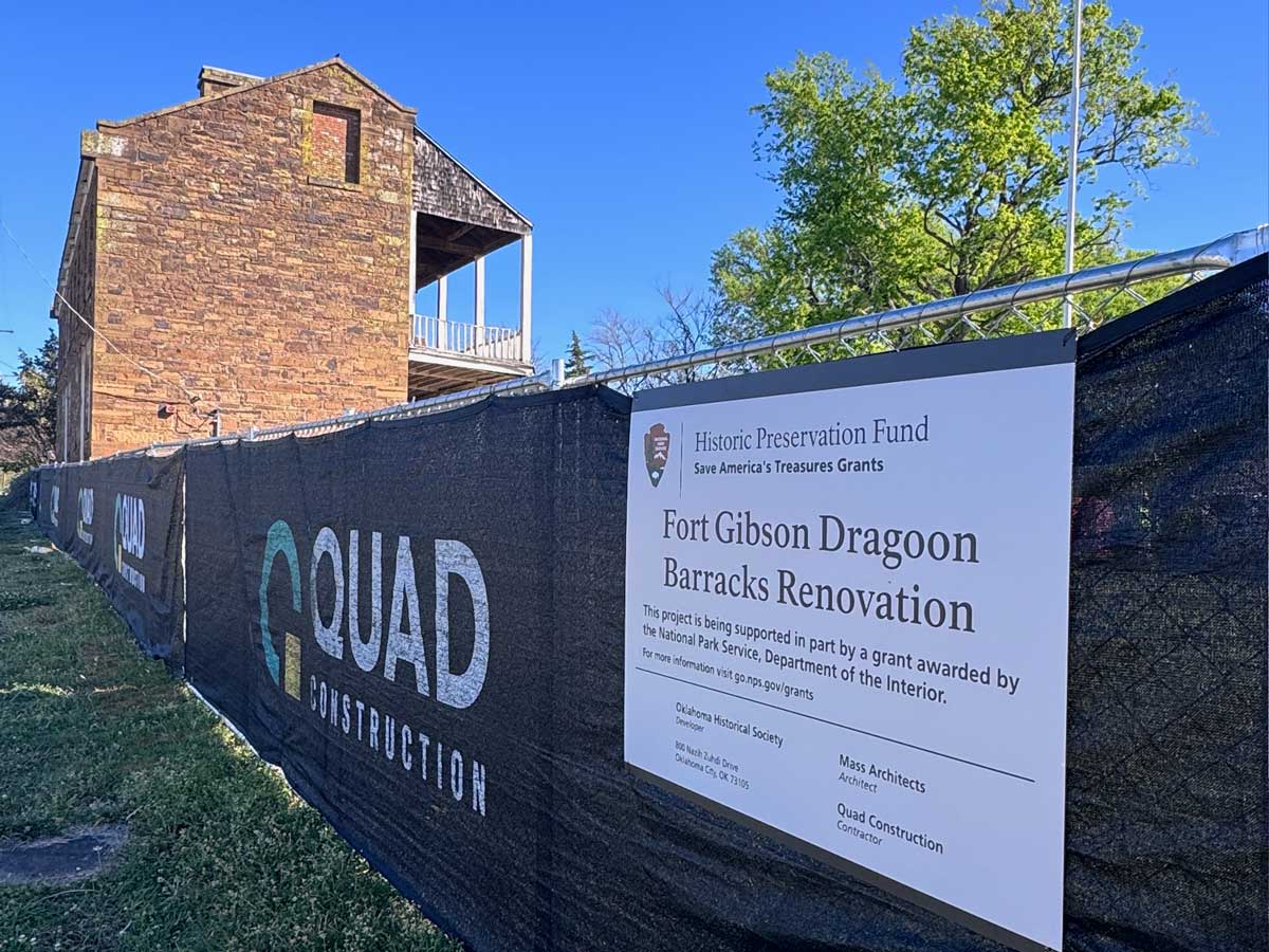 A temporary fence around the barracks renovation project with a sign crediting the National Park Service grant