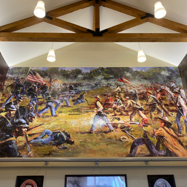 A section of a mural depicting the Battle of Honey Springs. The mural is visible below wooden beams and ceiling lights.